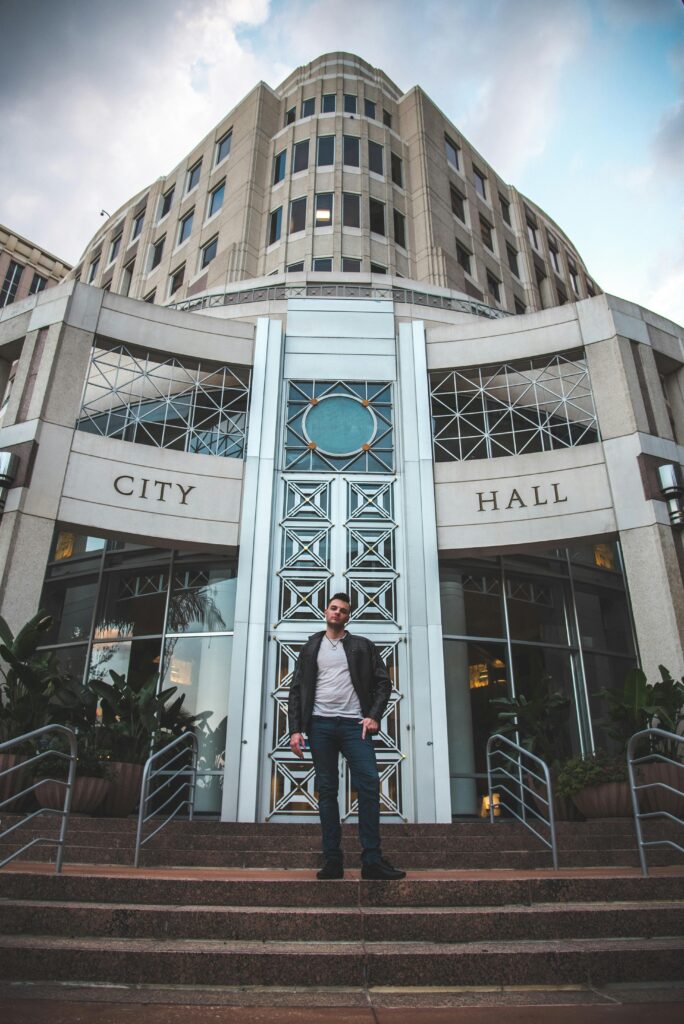 Stylish man in leather jacket and jeans standing outside city hall building.